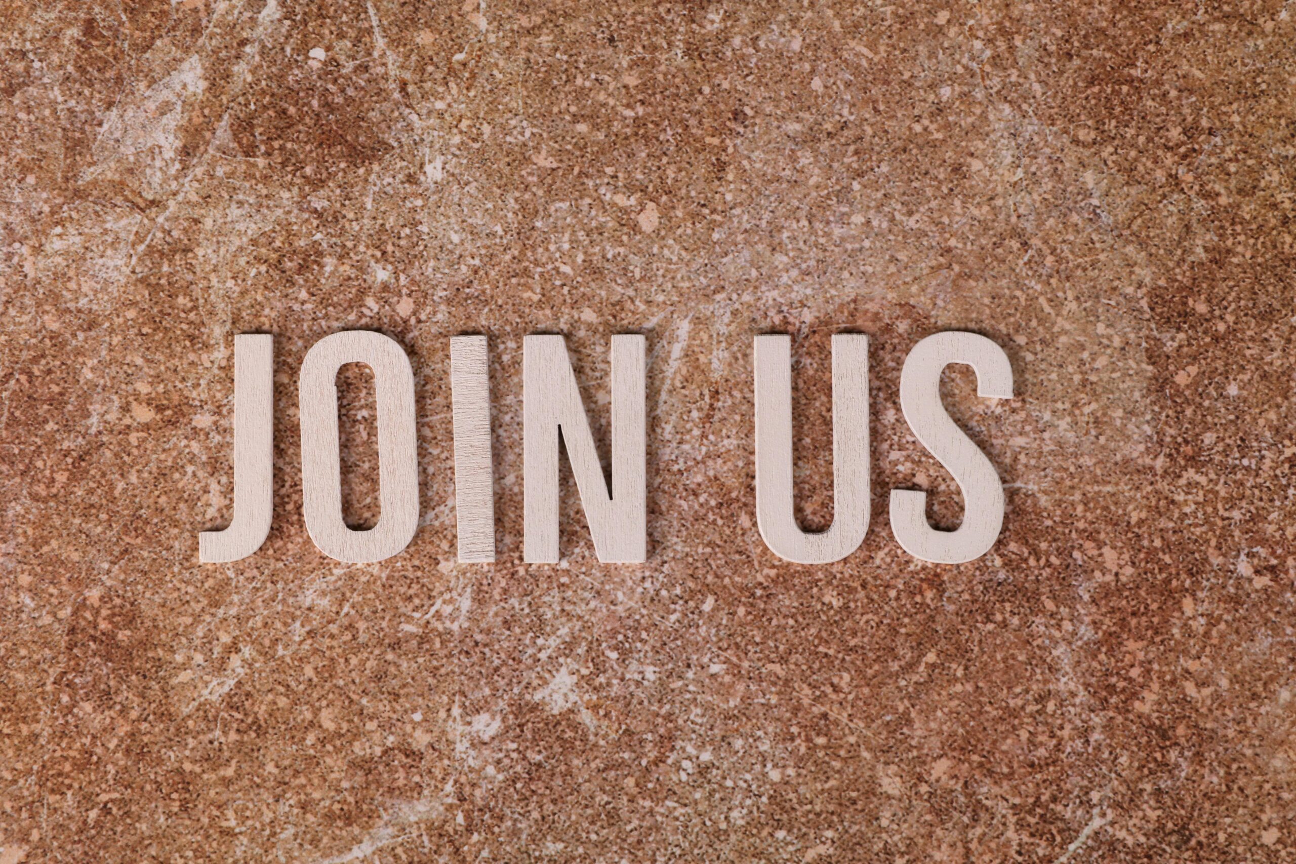 Wooden letters spelling 'Join Us' on a brown textured surface, suitable for invitations.